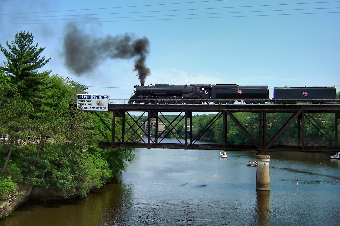 Steam locomotive and tender cars crossing a trestle bridge over a river.