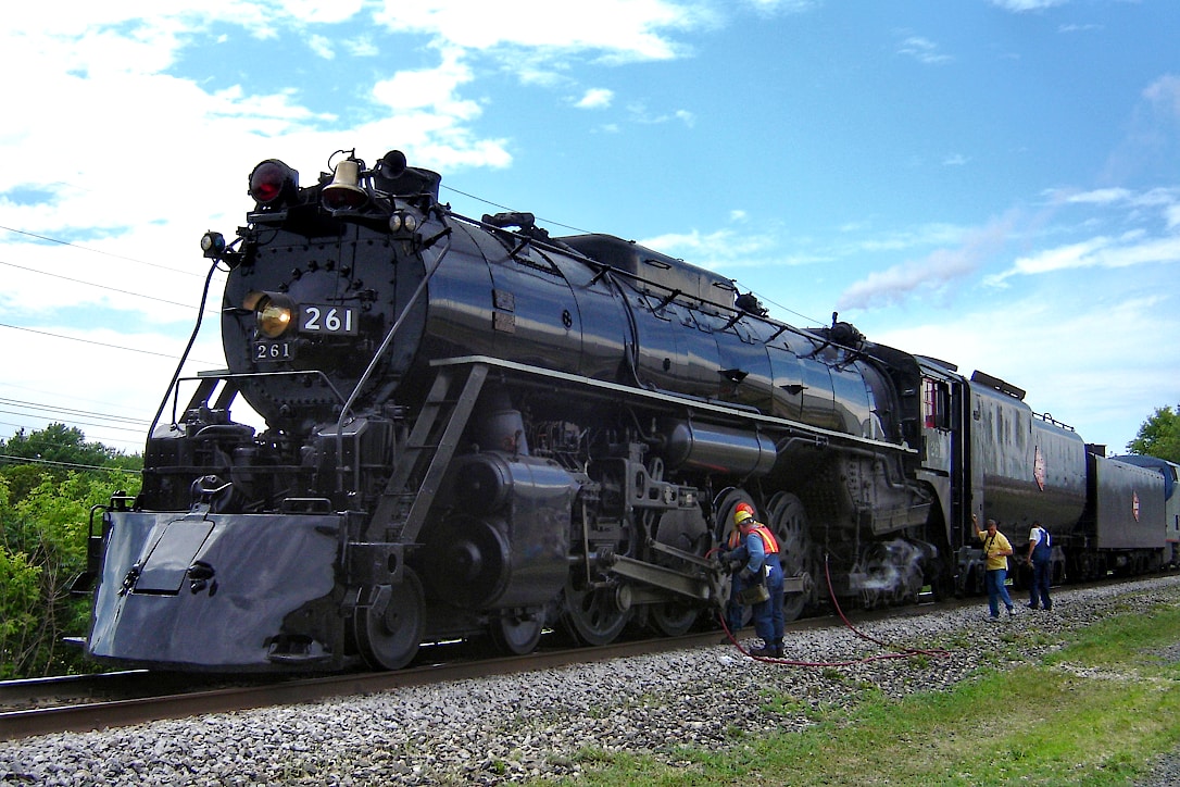 Locomotive 261 parked on the tracks while workers perform maintenance checks on the wheels.