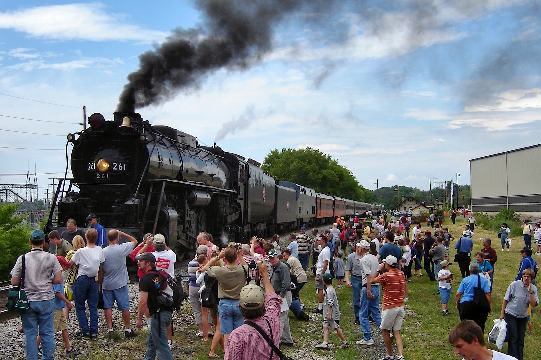 A large crowd in the grassy area next to a steam locomotive.