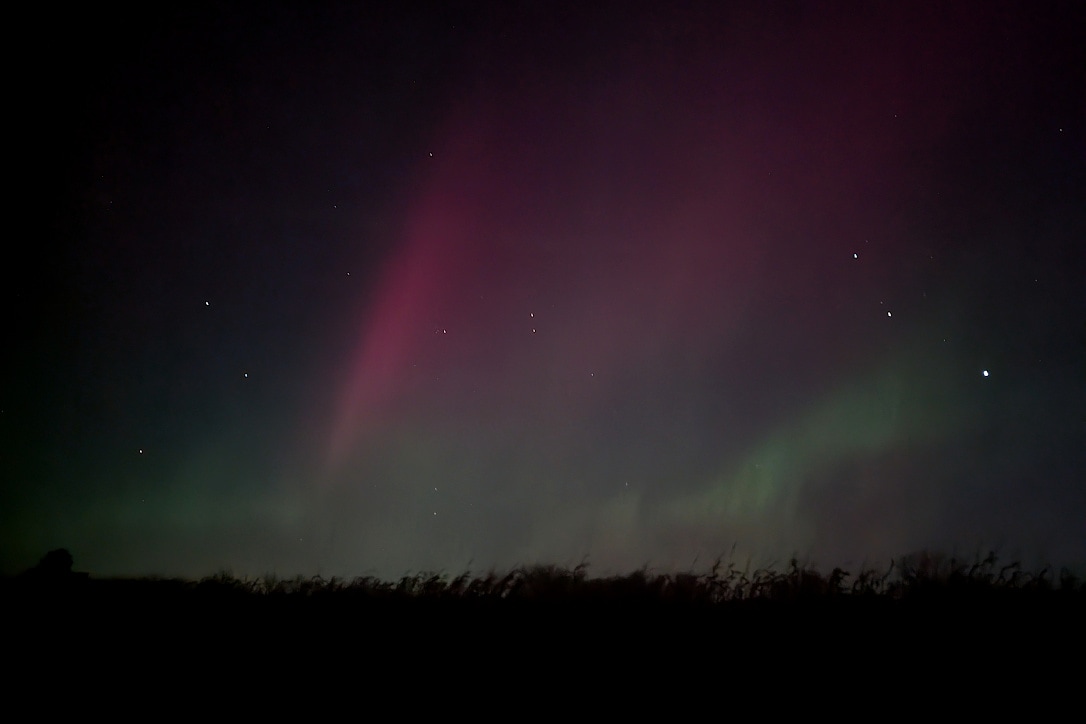 A few streaks of red and green light in the night sky with a few stars, above a prairie.