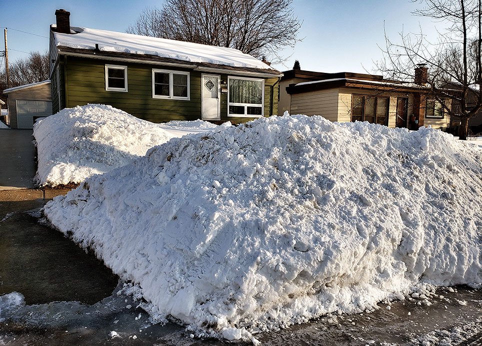 Snow piles along the street and driveway in front of a house