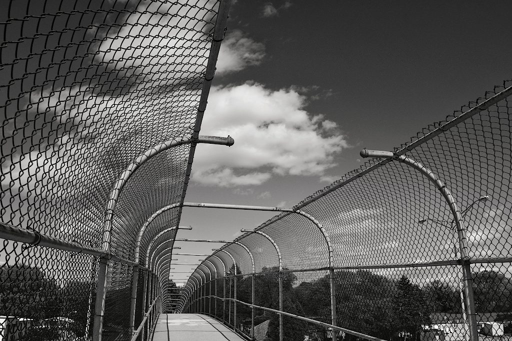 Partly cloudy sky above the top of a highway overpass with chain link fencing