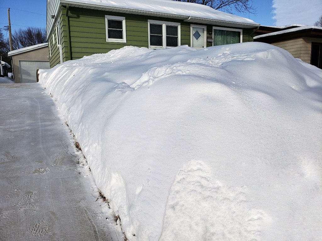 Snow piled high in front of a house next to a freshly shoveled driveway