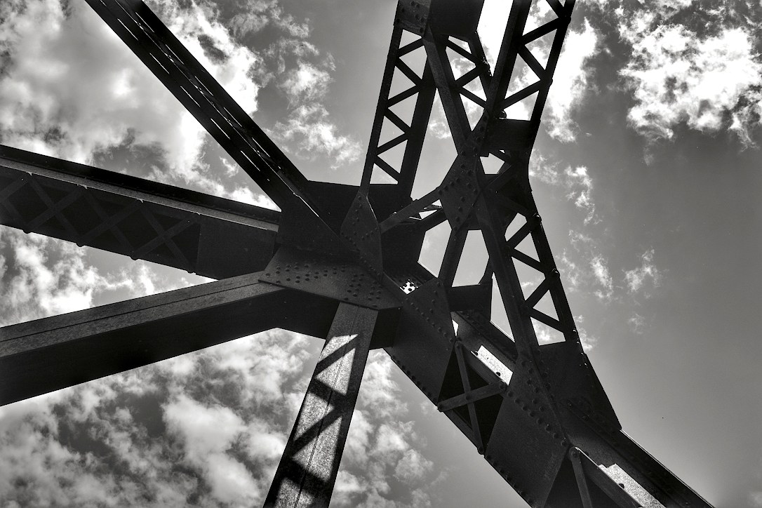 Looking up at several connected steel bridge girders in front of a partly cloudy sky