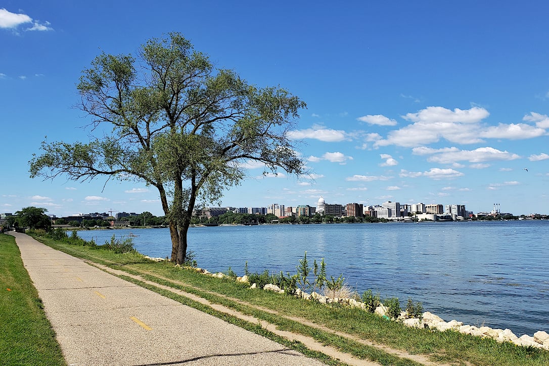 A recreational trail next to a lake with a view of the Madison skyline on opposite shore.