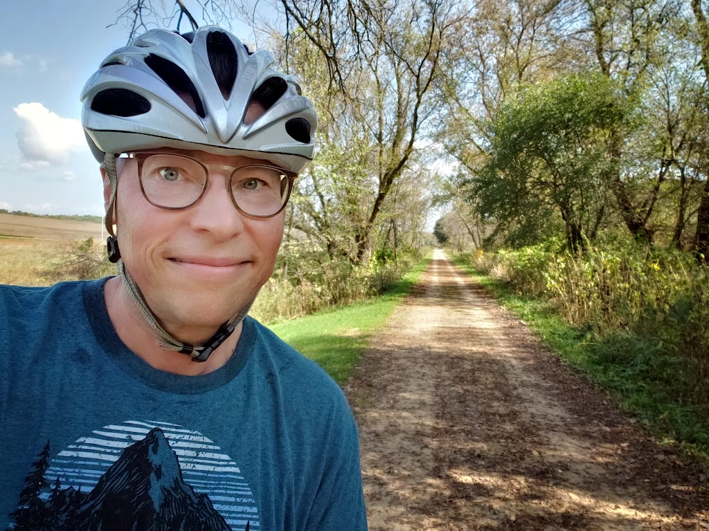 Jonathan Bloy wearing a bike helmet, next to a recreational trail that leads off into the distance
