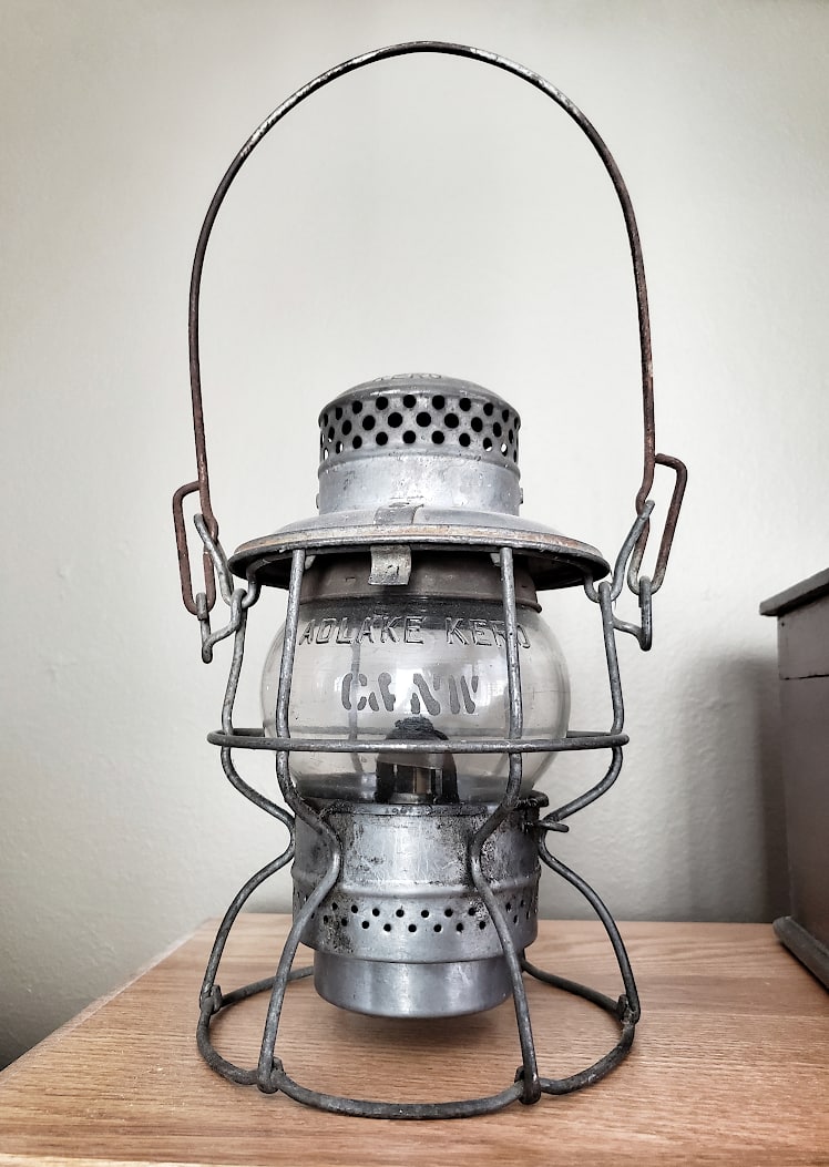 An antique railroad lantern standing on a table.