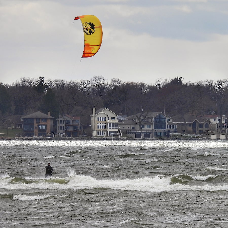 Person using a large kite to surf on a lake with whitecaps and rough water.