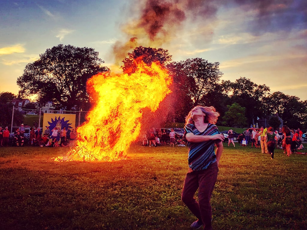 A woman dances in front of a large bonfire burning.