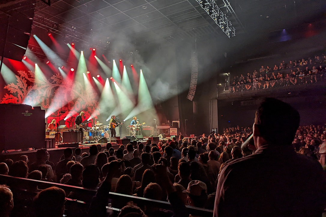 A music venue crowded with people, watches a band perform on stage under many small red and white spot lights.