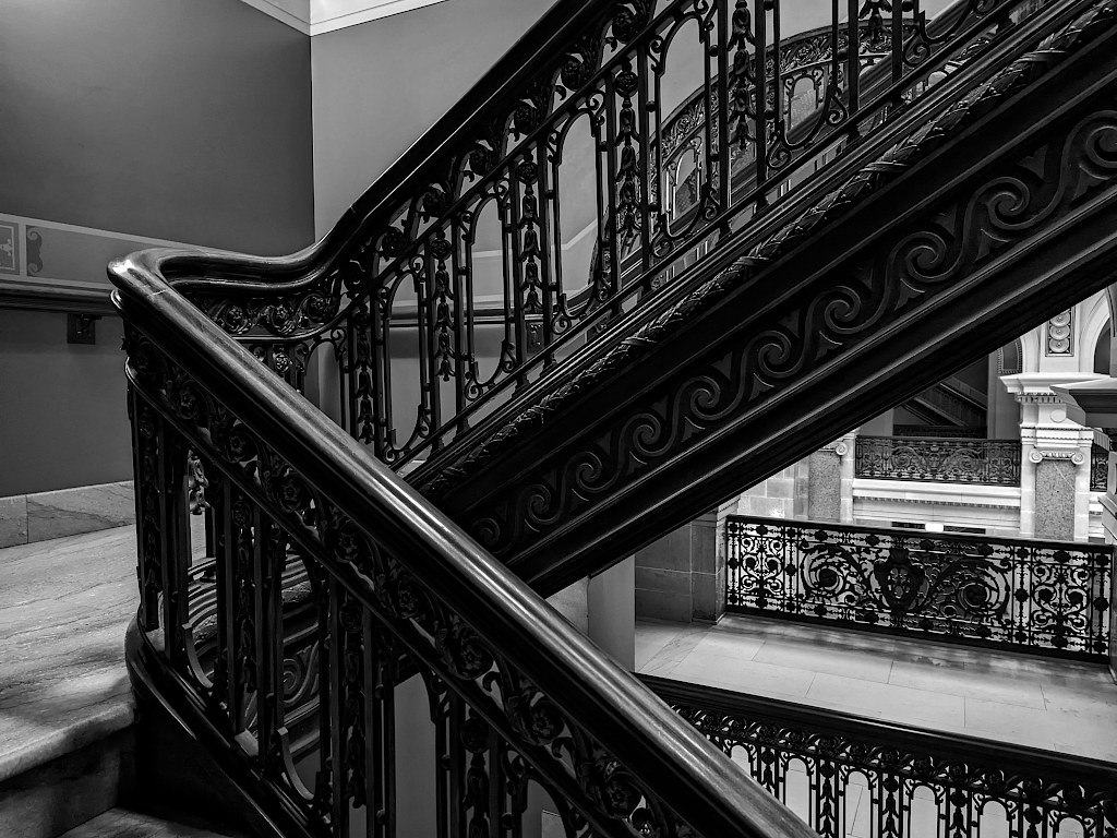 A very ornate wooden and wrought iron railing going up and down from a stairway landing.